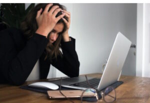 Woman in front of her computer grabbing her head with both hands